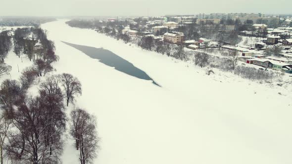 Snowy Winter Landscape with Frozen River and Suburbs Aerial View