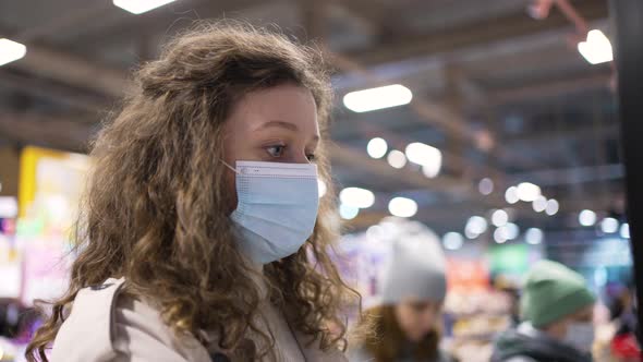 Curlyhaired Woman with Mask Chooses Cake in Supermarket