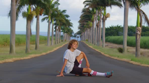 A Teenager with Long Hair Rides a Skateboard Along a Beautiful Road with Palm Trees