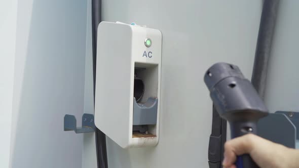 Hand pulling in cable from EV car charger or electric vehicle station. Cable connected