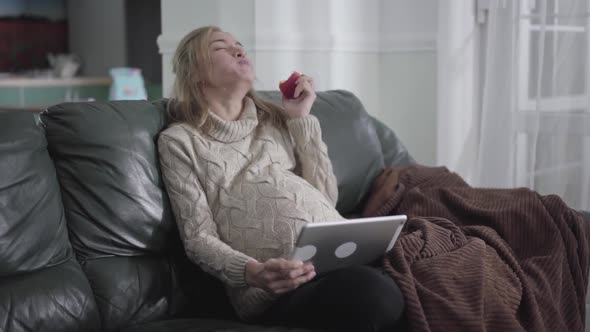 Beautiful Pregnant Caucasian Girl Eating Apple and Watching Video on Tablet