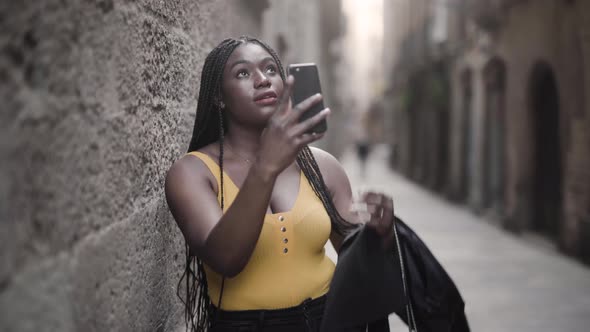 Ethnic woman taking photo of building on smartphone in town