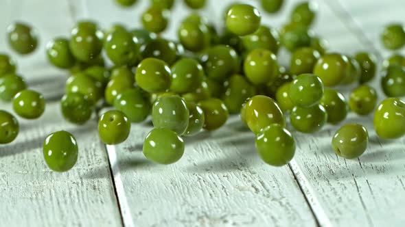 Super Slow Motion Shot of Rolling Fresh Green Olives on White Wooden Table at 1000 Fps