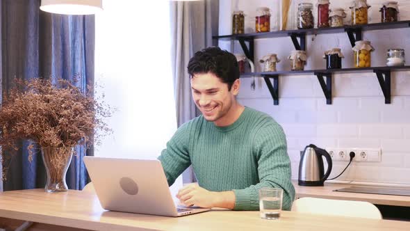 Online Video Chat By Young Man on Laptop Sitting in Kitchen