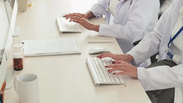 Two Female Doctor Typing on Computer Keyboards at Desk