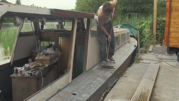 Youth brushing sanded deck of wooden boat