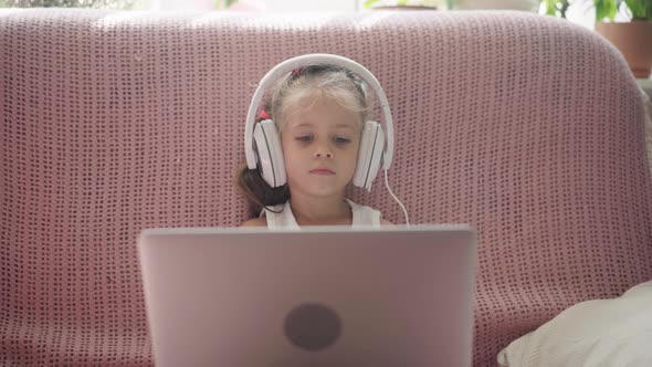 Little Girl Sitting Sofa in Headphones Listen Music Use Laptop Have Fun Home Interior Caucasian