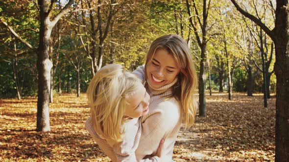 Young Mother is Smiling Holding Little Daughter in Her Arms and Circling Around During Their Walk in