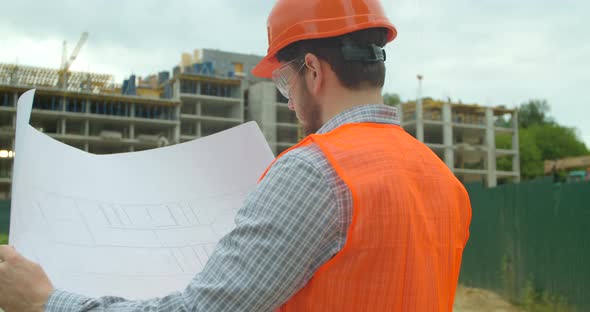 Close-up Portrait of Engineer with Blueprint on Background of Building Under Construction. Young