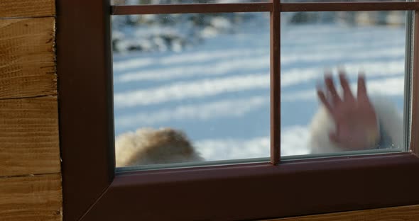 Child Playing Outdoors in Winter Snow Peering Into a Wooden House Through the Glass Window Pane in a