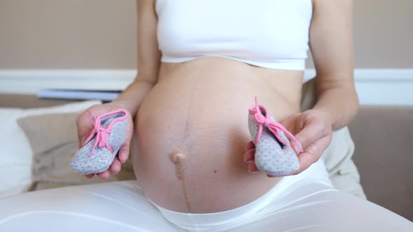 Closeup Of Pregnant Woman Holding Booties For Her Future Baby Near Her Belly