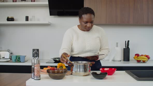 African Woman with Tablet Pc Trying New Recipe at Home