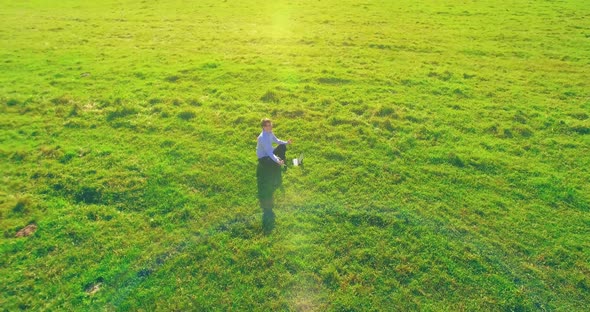 Low Orbital Flight Around Man on Green Grass with Notebook Pad at Yellow Rural Field