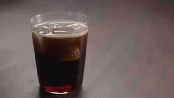 Slow Motion Man Pour Cola Over Ice Cubes Into Tumbler Glass on Walnut Table with Copy Space