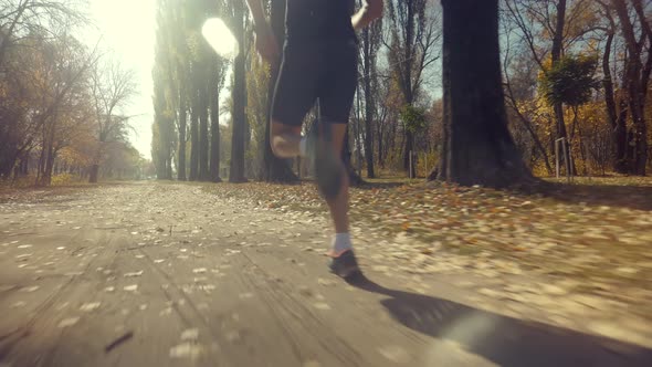 Running Man In Forest At Sunset. Runner Man Fit Athlete Legs Jogging On Trail Ready To Triathlon.