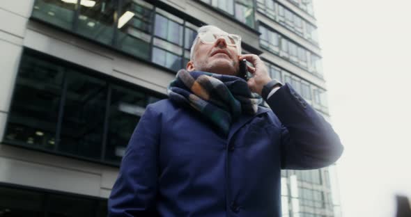 A Grayhaired Man Uses a Mobile Phone Standing in Business Center of the City