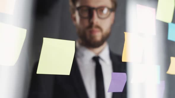 Man with Glasses in a Modern Office Writes a Word Deadline on the Glass Board with Sticky Notes