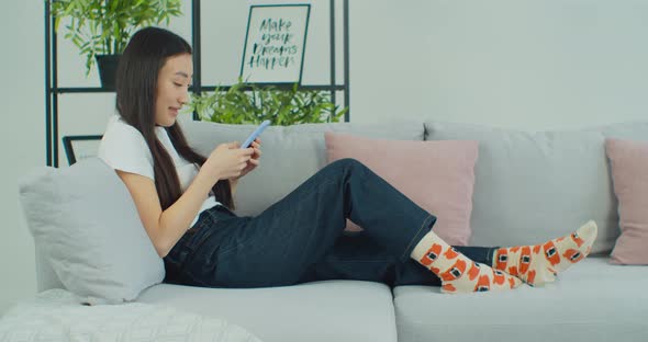Asian Woman Use Smartphone Application Sitting on Comfortable Sofa Technology Connection Concept