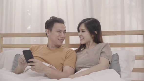 Asian couple using mobile phone while lying on the bed when relax in bedroom playing social media.