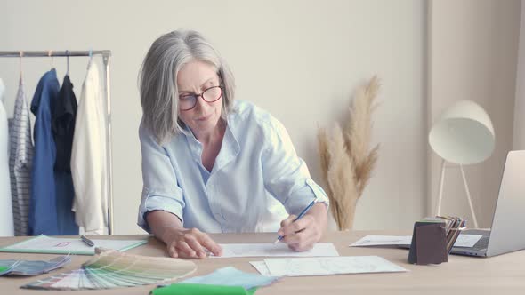 Mature Older Elegant Woman Fashion Designer Drawing Sketches on Table