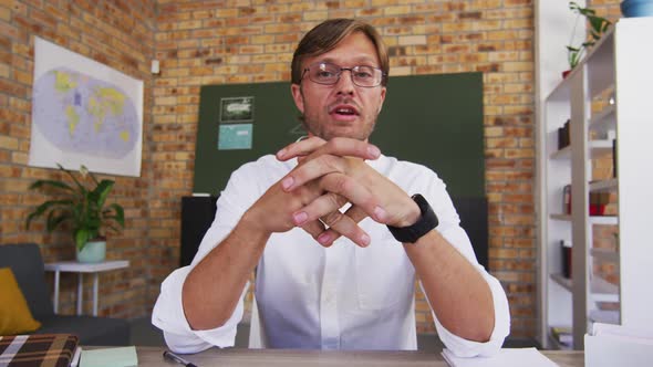 Portrait of caucasian male teacher teaching on videocall in the classroom at school