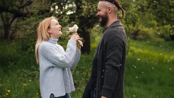 The Woman Is Standing with Her Boyfriend and Blowing on the Dandelion Flower in a Park