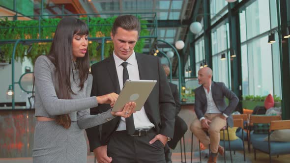 Businesswoman and businessman standing in office and discussing project on tablet computer