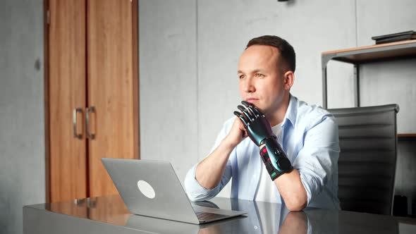 Disabled programmer with high temples and bio hand prothesis sits at table