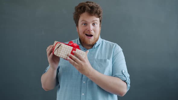 Portrait of Happy Guy Holding Birthday Present Shaking Gift Box Looking at Camera with Happiness and
