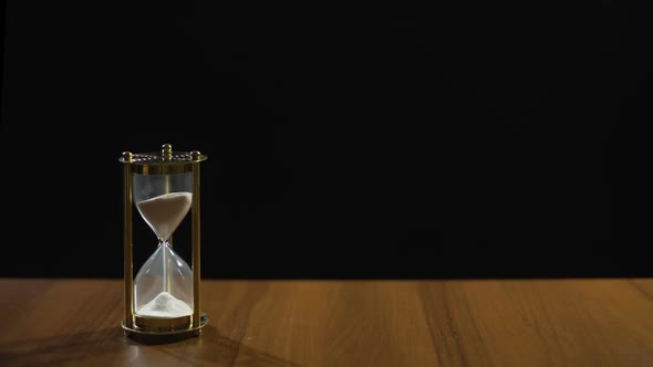 Sand Flowing Fast in Hourglass on Table Against Black Background, Time Flies