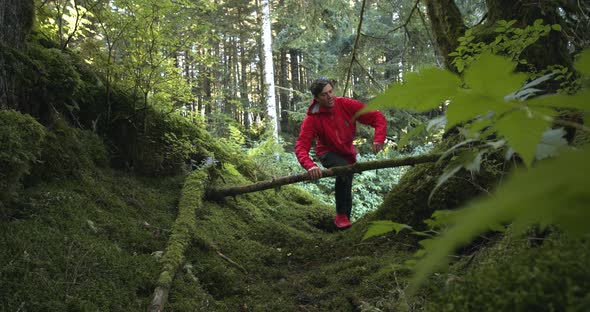 Adult Man In Red Jacket And Shoes Running, Jumping Over A Fallen Tree Branch In A Forest Trail In Al