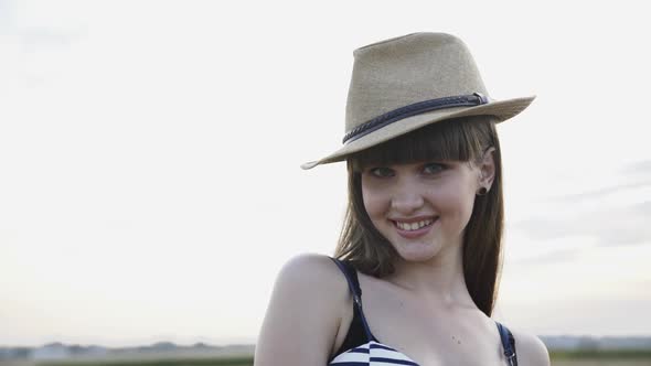 Portrait of Seductive Girl in Hat Poses and Flirts at Camera with Smile