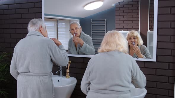 Senior Couple Man and Woman Brushing Teeth and Looking Into a Mirror at Luxury Bathroom at Home