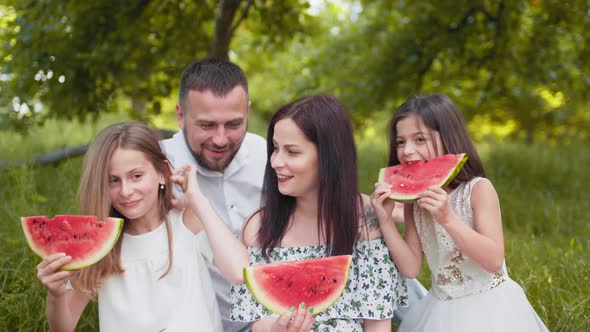 Joyful Caucasian Family with Two Little Daughters Eating Watermelon Outdoors