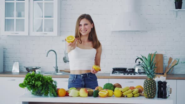 Beautiful female in the light kitchen. Smiling young woman proposing fresh orange.