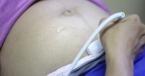 Close up of male doctor holding ultrasound transducer to pregnant belly while examining expectant yo