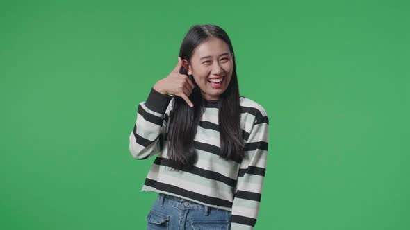 A Cheerful Asian Woman Making A Phone Call Hand Gesture While Standing In Front Of Green Screen