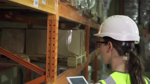 Rear View of a Female Worker in a Protective Vest and Helmet As She Walks Through the Warehouse