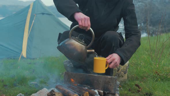 Man making cup of coffee solo camping by fire 4K