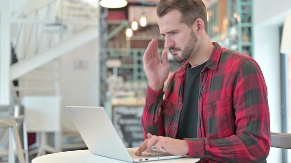 Young Man with Headache Using Laptop in Cafe