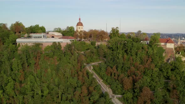 Aerial view flying pull away from landmark Glokenturm tower on Graz's Schloßberg hilltop woodland pa