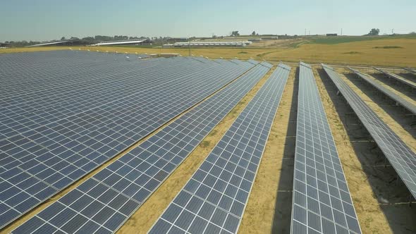 Aerial footage of hundreds solar energy modules or panels rows along the dry lands