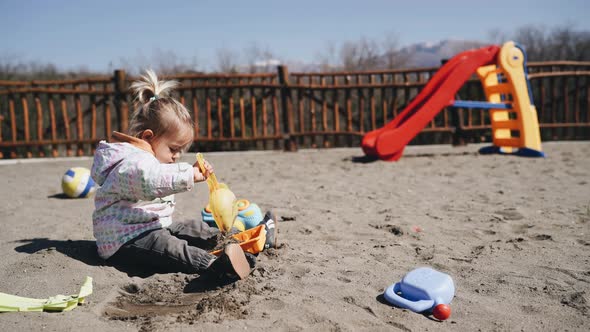 Little Girl Playing with Shovel and Sand in the Playground