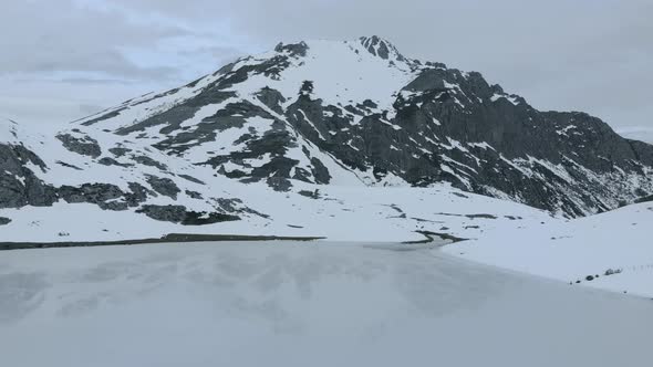 Aerial Drone Top notch fly Snowy dim Mountain frozen Lake Cloudy sky in Isoba Lake, Leon Asturias, S