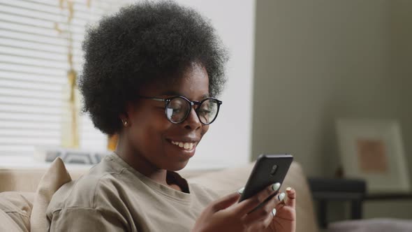 Cheerful Black Woman Using Smartphone at Home