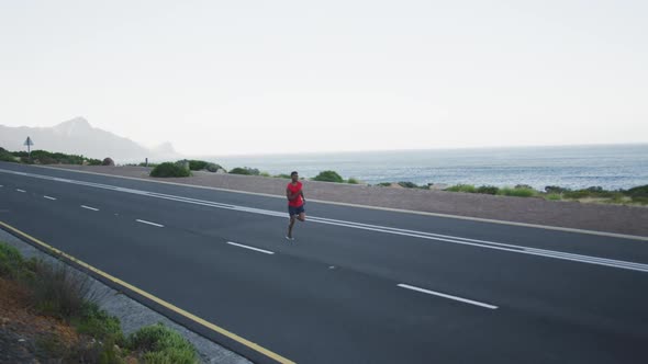 African american man exercising outdoors running on a coastal road