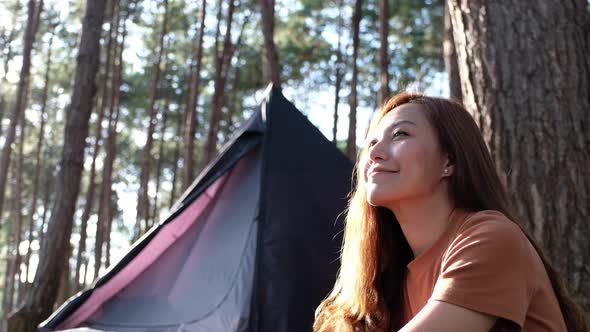 A young asian woman sitting next to a tent while enjoy camping in the outdoors