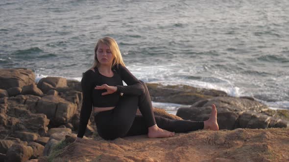 Pretty Girl in Black Tracksuit Sits on Grey Rocky Cliff