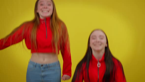 Two Joyful Excited Twin Sisters Jumping Up at Yellow Background Laughing