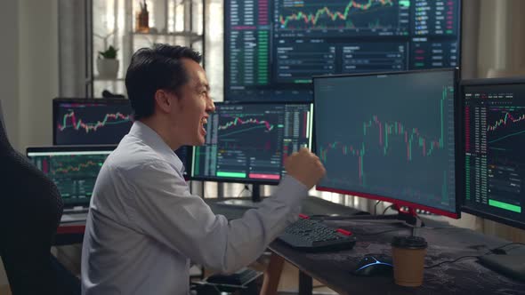 Asian Male Stock Market Broker Happy With Analyzing Graphs On Multiple Computer Screens